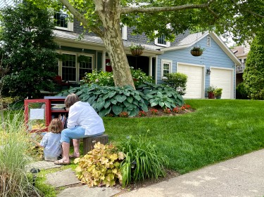 Grandmother and grand daughter looking at a community book library on a front lawn.